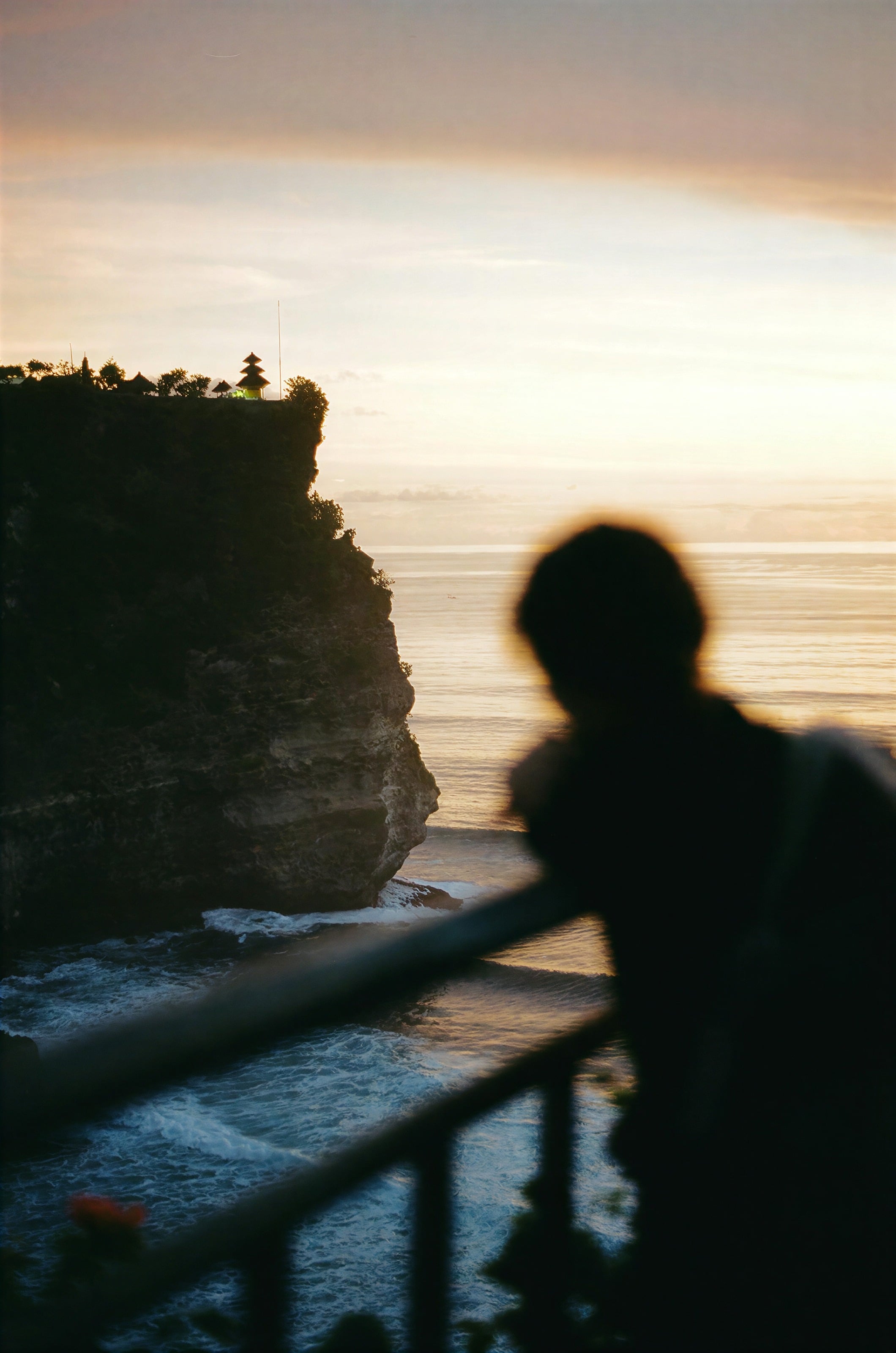Una silueta en una barandilla sobre los acantilados al atardecer en Bali