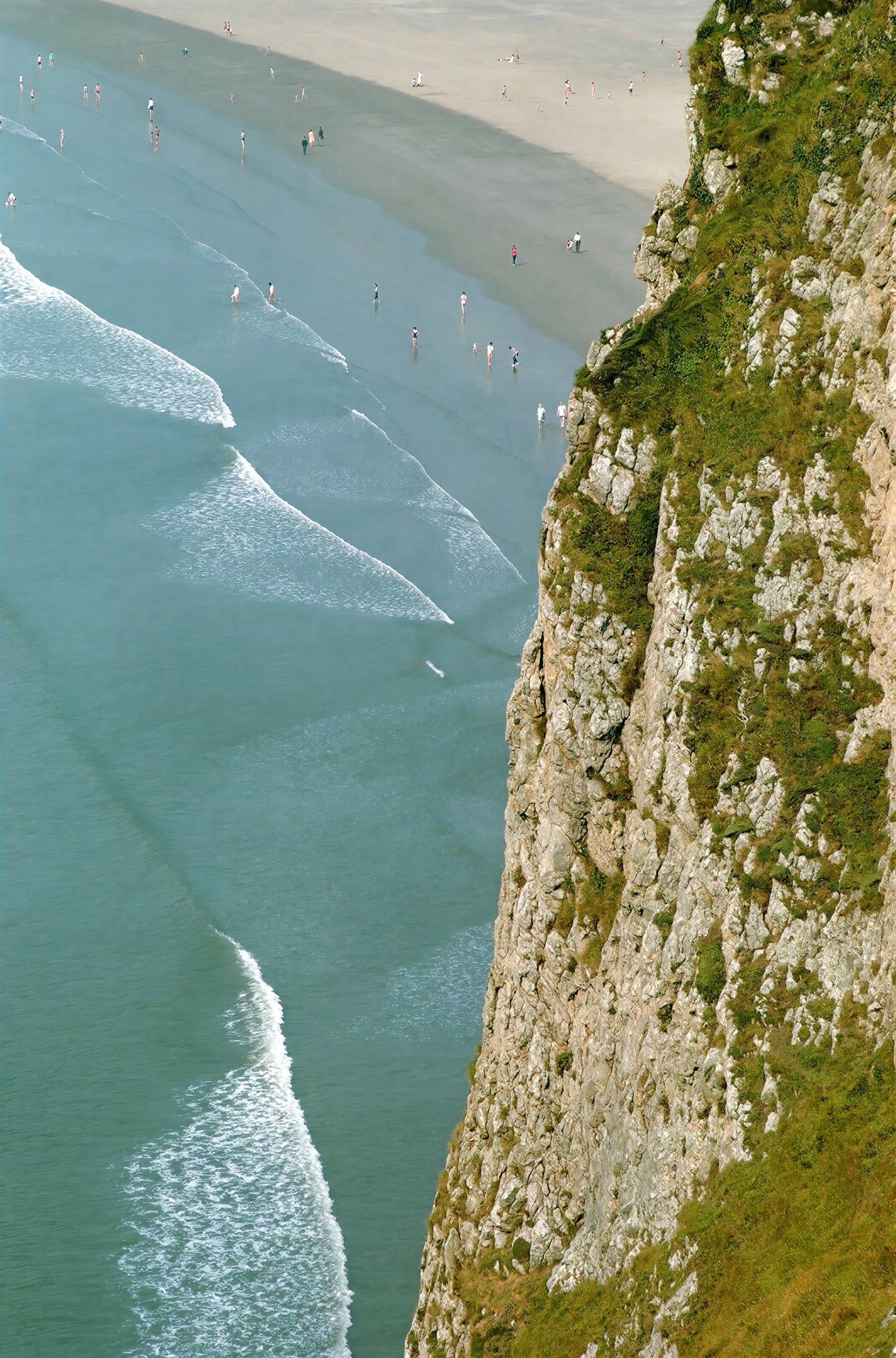 Olas llegando a una playa bajo un acantilado verde, vistas desde arriba