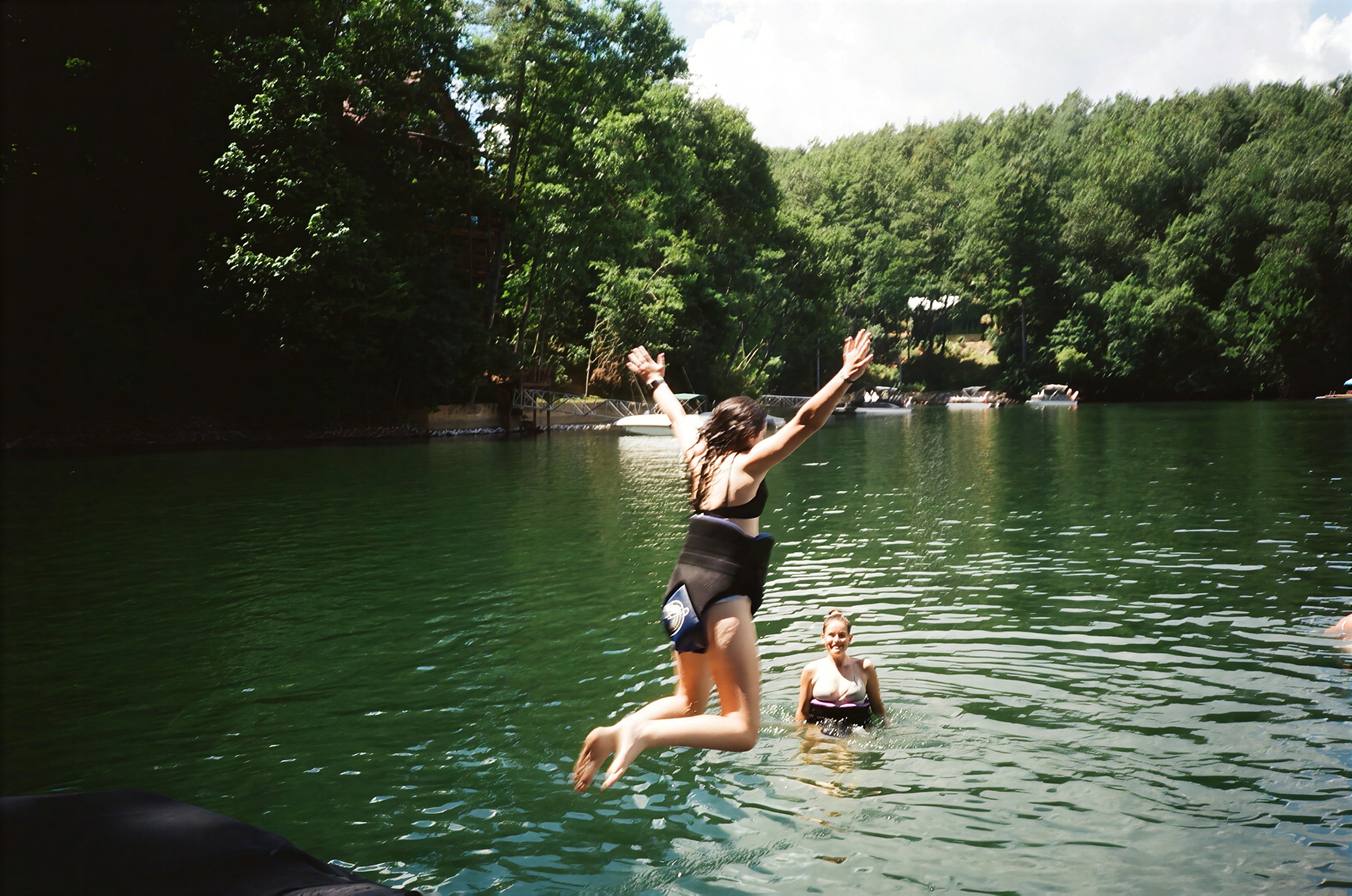 Una huésped saltando a un lago del bosque mientras una amiga nada cerca